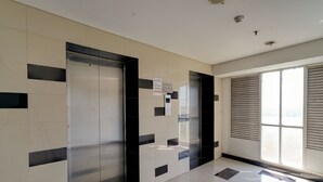 A modern elevator with a control panel, a tiled floor, and a large window with blinds. - OYO Life 92889 Apartement Grand Sentraland Karawang By A.t Room (Karawang)