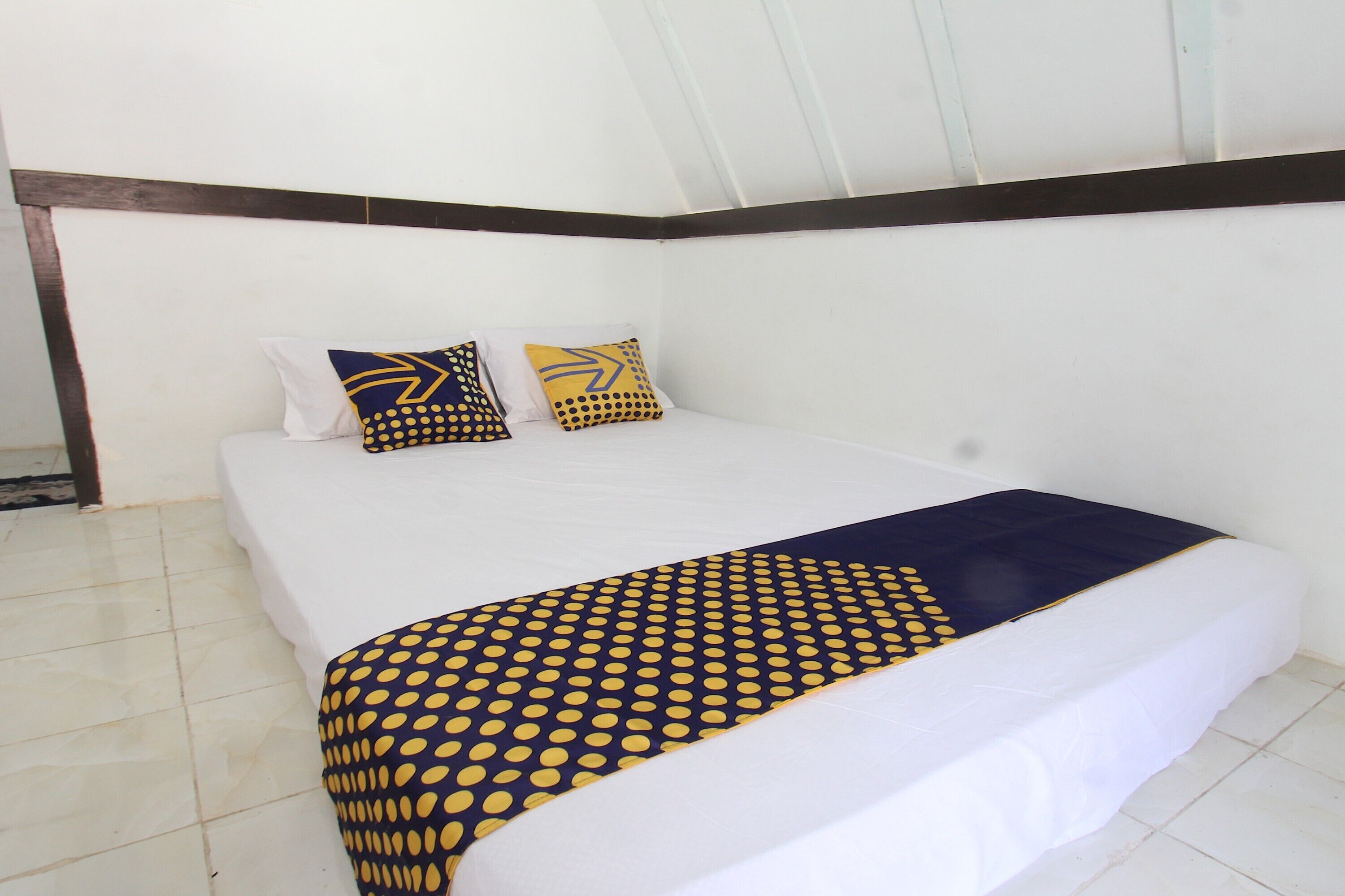 A neatly made bed with a white mattress, a blue and yellow patterned blanket, and two pillows with similar designs.