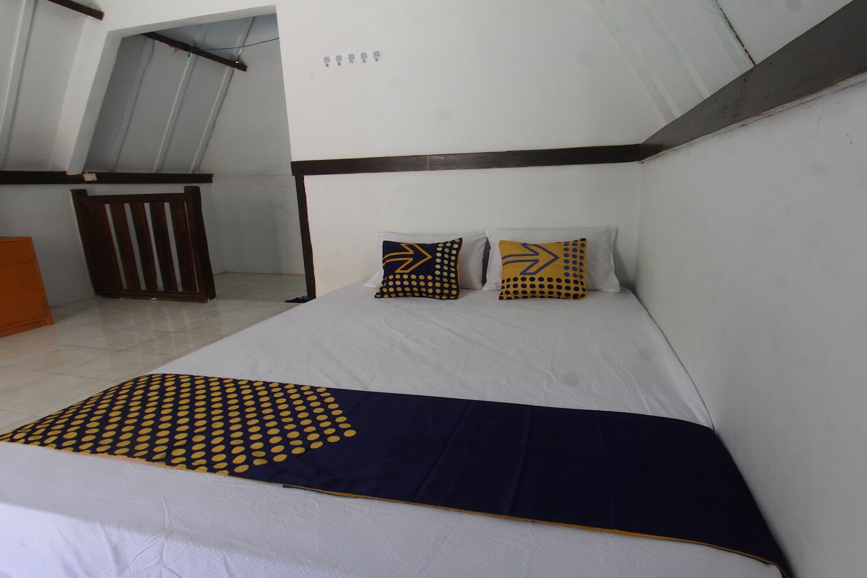 Un dormitorio con una cama, dos almohadas de diseños geométricos, un edredón azul oscuro y una silla de madera.