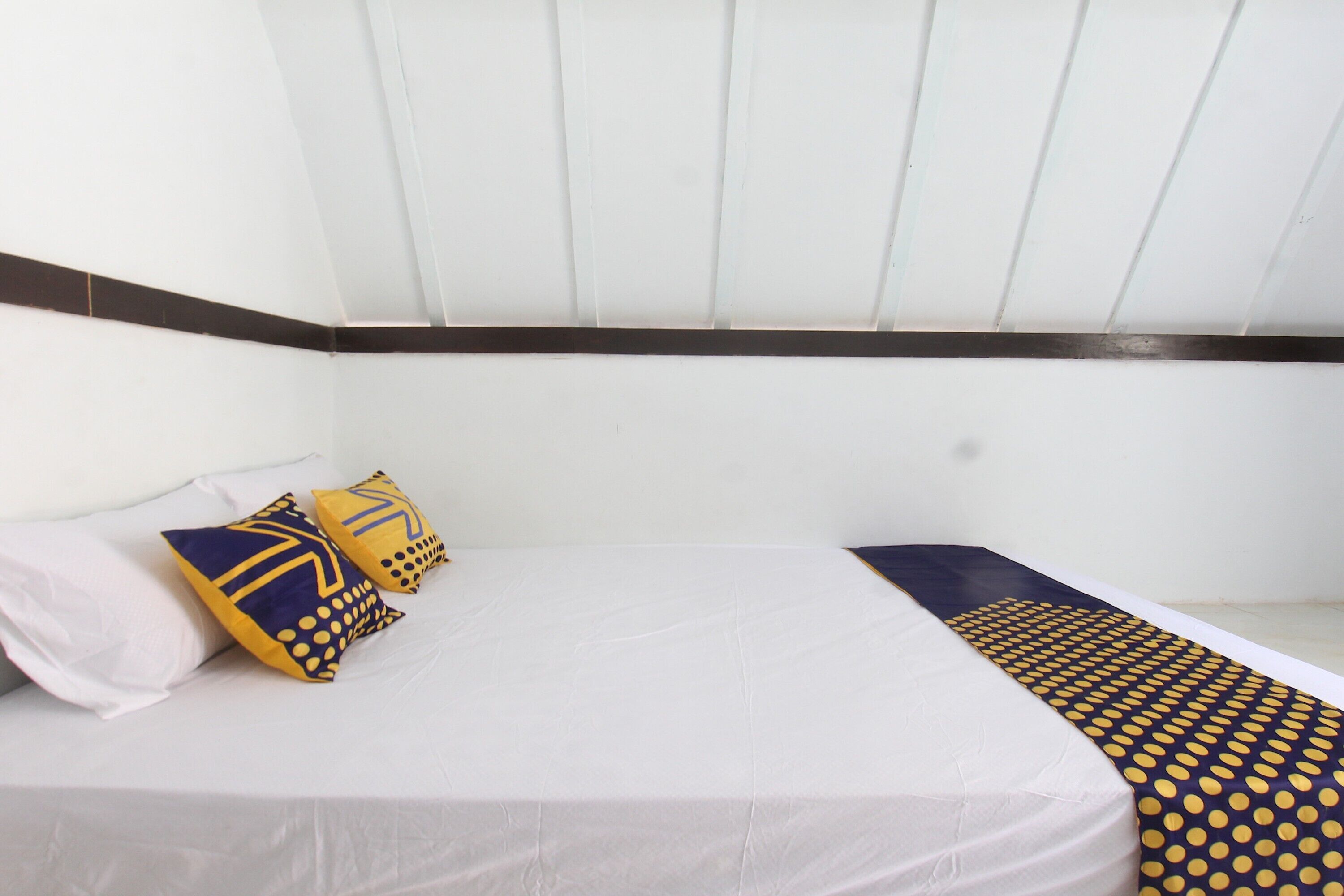 A bed with white bedding and two decorative pillows, one with a geometric pattern and the other with a polka dot design.