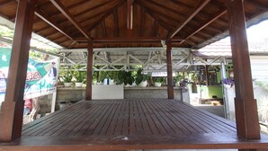 A covered wooden deck with a metal roof structure, surrounded by potted plants and a concrete wall.