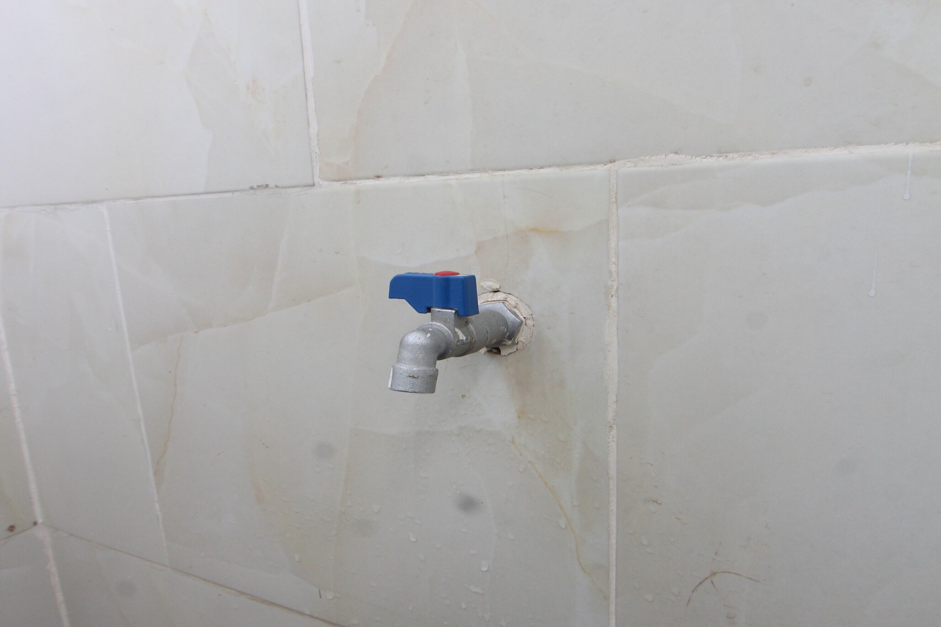 A bathroom with a visible water spigot and a damaged wall.