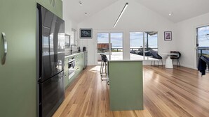 A modern kitchen with a large island, wooden flooring, and a view of the outdoors. - RARE Views - Diamond Skies - Incredible! (Glamorgan-Spring Bay)