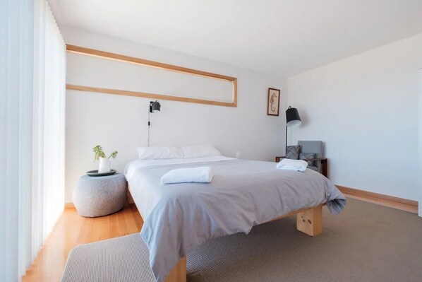 A modern bedroom with a large bed, bedside tables, a lamp, and a framed picture on the wall.