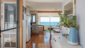 A modern kitchen with a view of the sea, wooden flooring, and a dining area with a large plant. - AWESOME Beach House Bicheno (Glamorgan-Spring Bay)