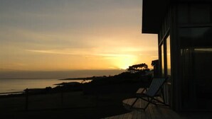 A sunset view from a balcony with a chair and a wooden deck. - AWESOME Beach House Bicheno (Glamorgan-Spring Bay)