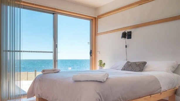 A bedroom with a large bed, a view of the sea, and a sliding glass door to the outside. - AWESOME Beach House Bicheno (Glamorgan-Spring Bay)