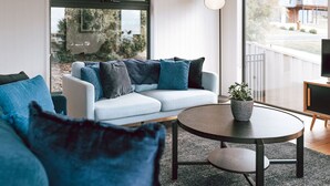 Ein modernes Wohnzimmer mit einem weißen Sofa, blauen Kissen, einem runden Couchtisch und einem Topfpflanzen.