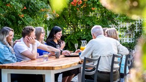 A group of people seated around a wooden table outdoors, engaged in conversation.