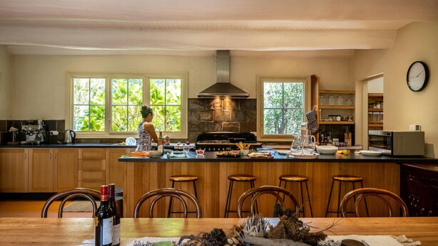 A kitchen with a central island, wooden bar stools, and a dining table with a bottle of wine.
