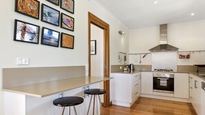 Una cucina moderna con isola centrale, sgabelli da bar, cappa aspirante in acciaio inossidabile e schienale decorato con un motivo geometrico.