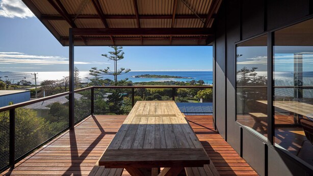 A wooden deck with a table and chairs, overlooking a scenic view of the ocean and distant land. - Lucy (Glamorgan-Spring Bay)