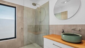 A modern bathroom with a glass shower enclosure, a round mirror, and a wooden vanity with a green sink. - Lucy (Glamorgan-Spring Bay)