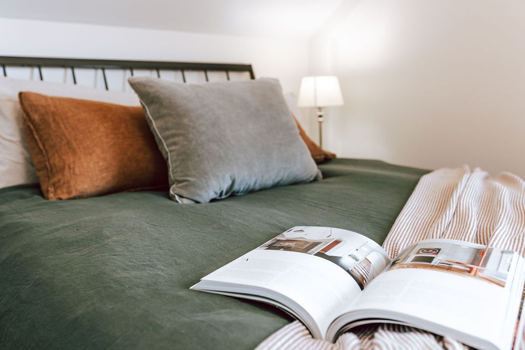 A neatly made bed with a green bedspread, two pillows, and an open magazine on the bed.