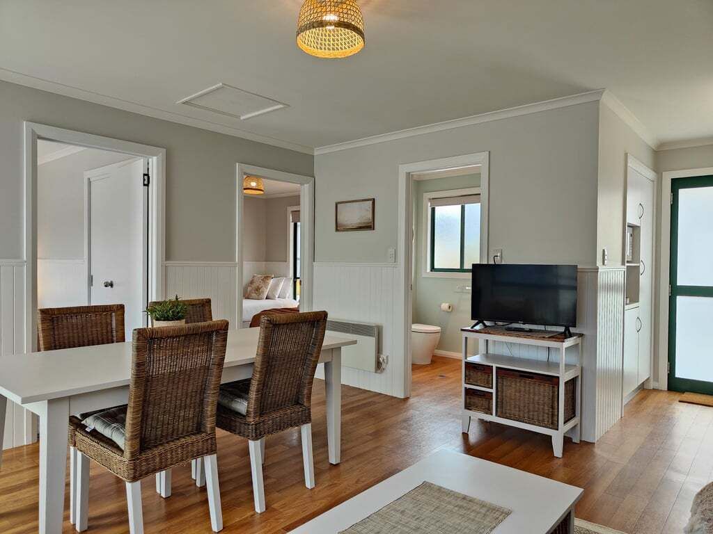 A modern living room with a dining area, a television on a stand, and a view of the outside.