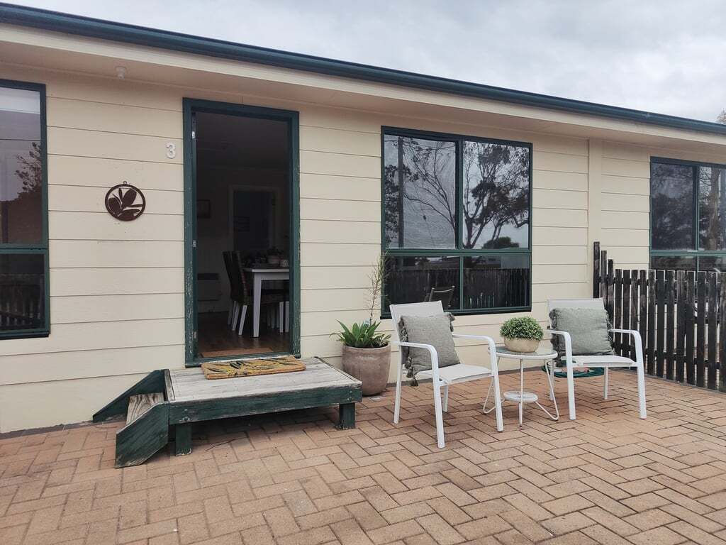 A building with a beige exterior, a door, and a small outdoor seating area with two chairs and a table.