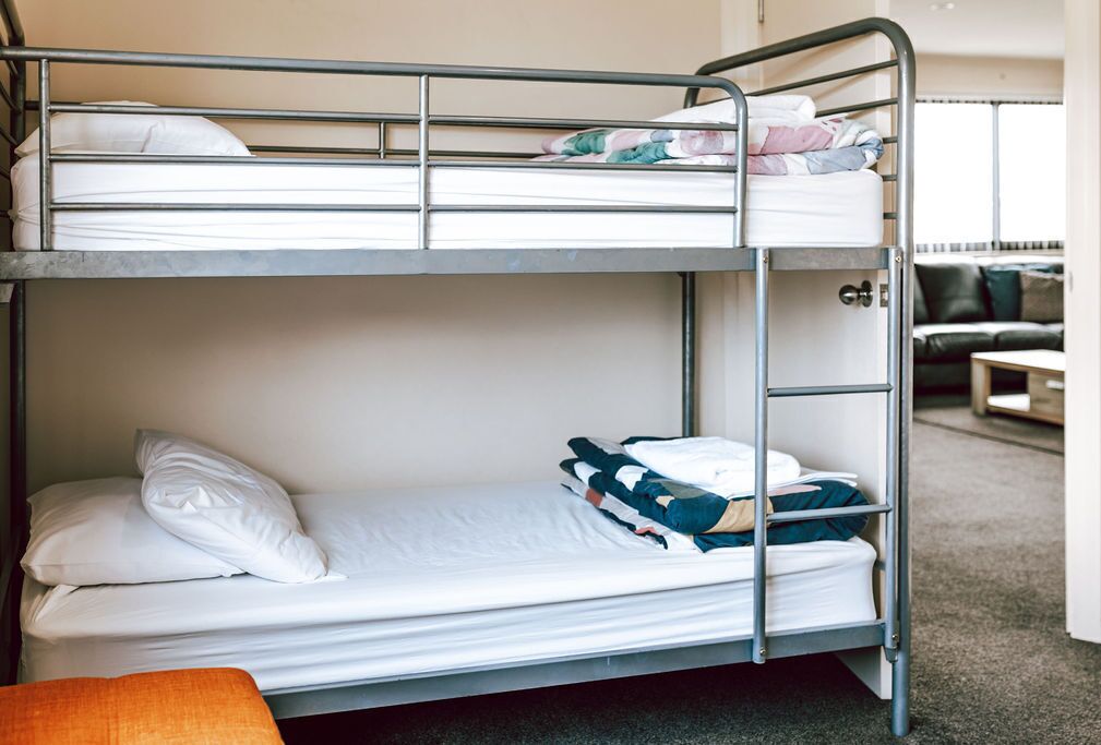 A bunk bed room with a metal frame, a white mattress on the top bunk, and a single bed on the bottom.