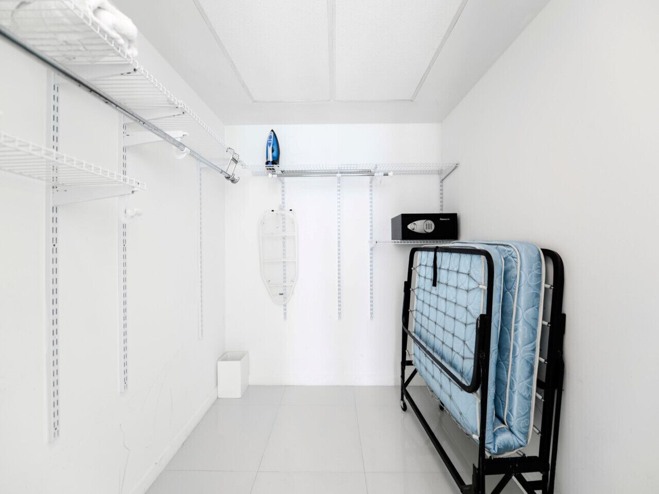 Una habitación limpia y blanca con estanterías metálicas, un tendedero y una estructura de cama de metal negro.