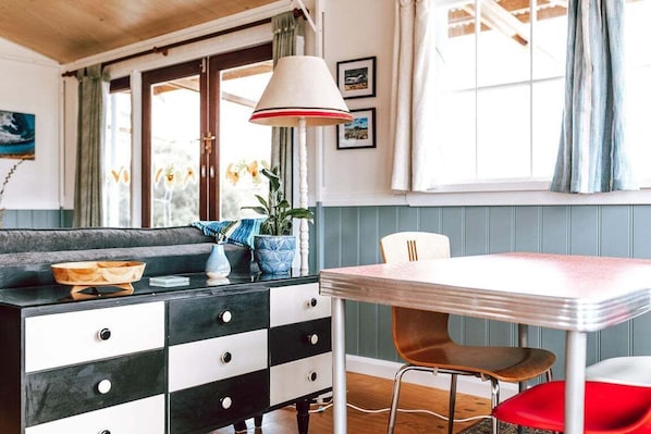 Un coin repas avec une table et des chaises, une commode noire et blanche, et une fenêtre avec des rideaux.