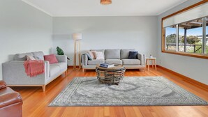 Un salon moderne avec un canapé gris, une table basse ronde et une grande fenêtre donnant sur l’extérieur.