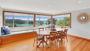 Un espace repas doté d’une grande fenêtre donnant sur un paysage pittoresque, d’un plancher en bois et d’une table ronde entourée de chaises.