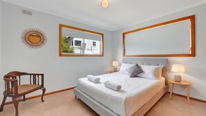 Une chambre à coucher avec un grand lit, deux tables de chevet, une chaise, un miroir et un motif décoratif représentant un soleil sur le mur.