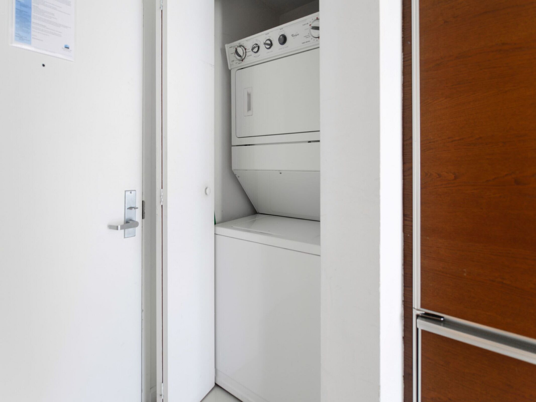 A laundry room with a white washing machine and dryer, a wooden door, and a white wall with a door handle.
