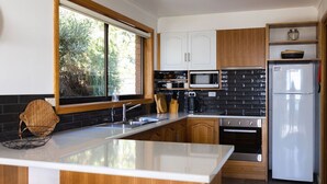 Een moderne keuken met een centraal eiland, houten kastjes, een inbouwoven, een magnetron en een koelkast.