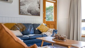 Een woonkamer met een blauwe bank, een houten salontafel en een deur met uitzicht op groen.