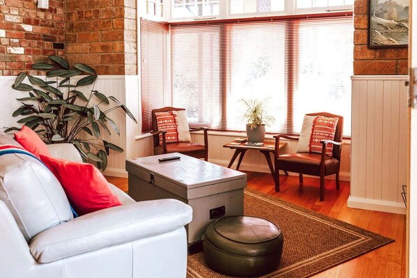 A living room with a white sofa, a coffee table, a leather ottoman, two armchairs, a potted plant, and a brick wall.