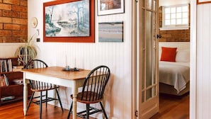 Une pièce comprenant une table à manger en bois, deux chaises, une bibliothèque et un lit près d’une fenêtre.