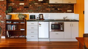 A modern kitchen with a brick wall, white cabinetry, a built-in oven, and a coffee maker. - The most beautiful guest retreat (Break O'Day)