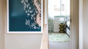 A hallway with a framed artwork on the wall, a carpeted floor, and a doorway leading to a room with a bed and a lamp. - KAL's House - The place to be! (Glamorgan-Spring Bay)
