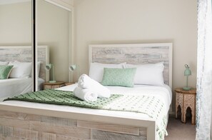 A neatly made bed with a green blanket and pillows, a bedside lamp, and a small wooden side table with a lamp.