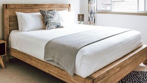 A wooden bed with white bedding, a patterned pillow, a bedside lamp, and a view of a building through a window. - KAL's House - The place to be! (Glamorgan-Spring Bay)