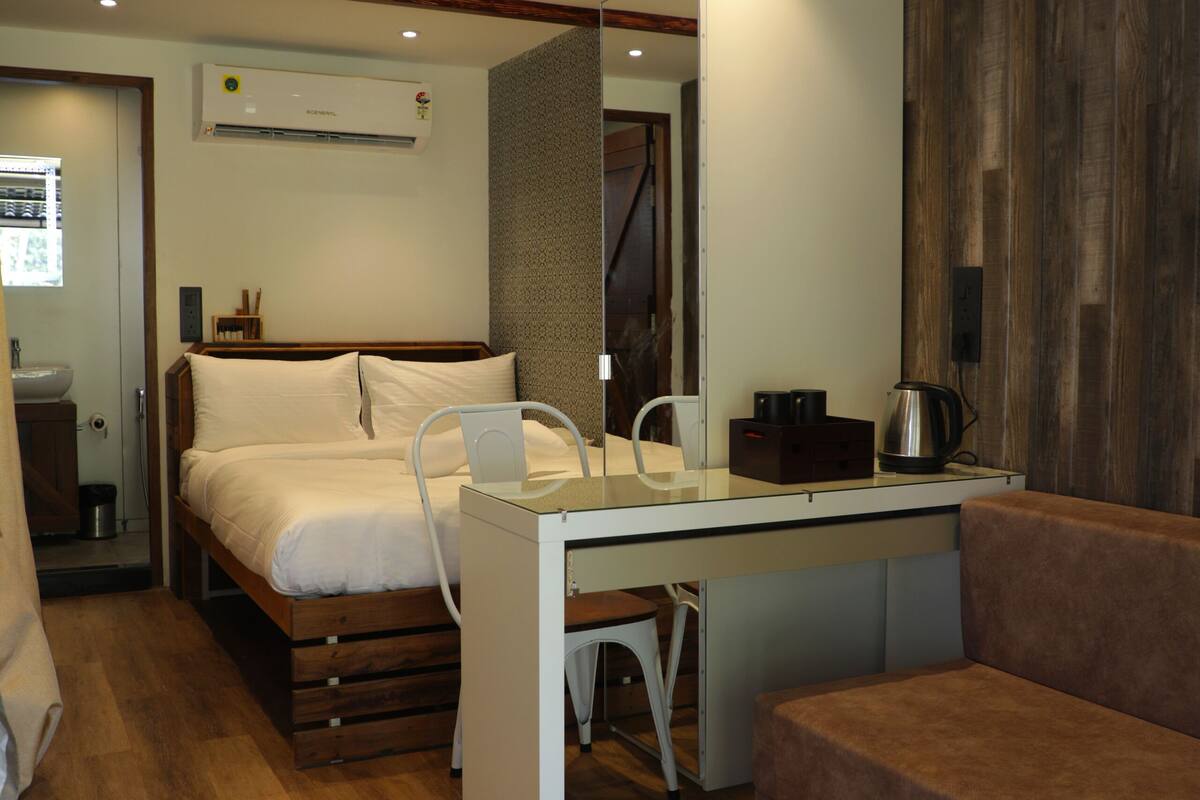 A compact hotel room with a bed, a desk, a chair, a sofa, and a mirror.