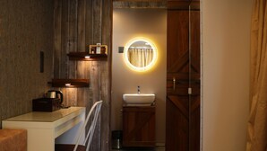 Une salle de bain moderne et compacte, dotée d’un meuble-lavabo en bois, d’un évier et d’un miroir avec un éclairage circulaire.