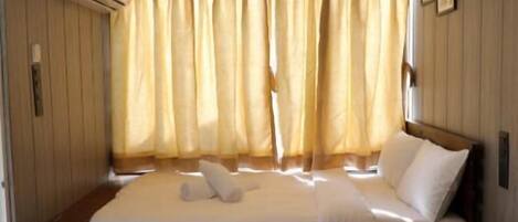 A bedroom with a wooden bed, a bedside table, a chair, and a window with curtains.