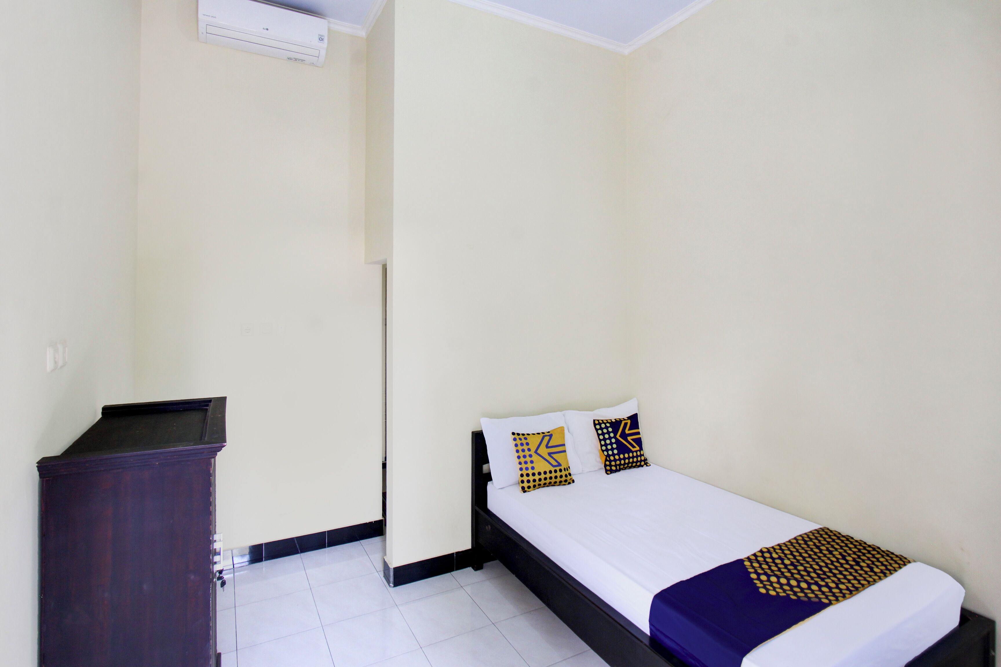 A small, clean room with a bed, a dresser, and a wall-mounted air conditioner.