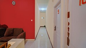 A hallway with a red wall, a white door with the number 10, and a brown couch. - OYO Life 92546 Kost Merah Bojongsoang Syariah (Bojongsoang)