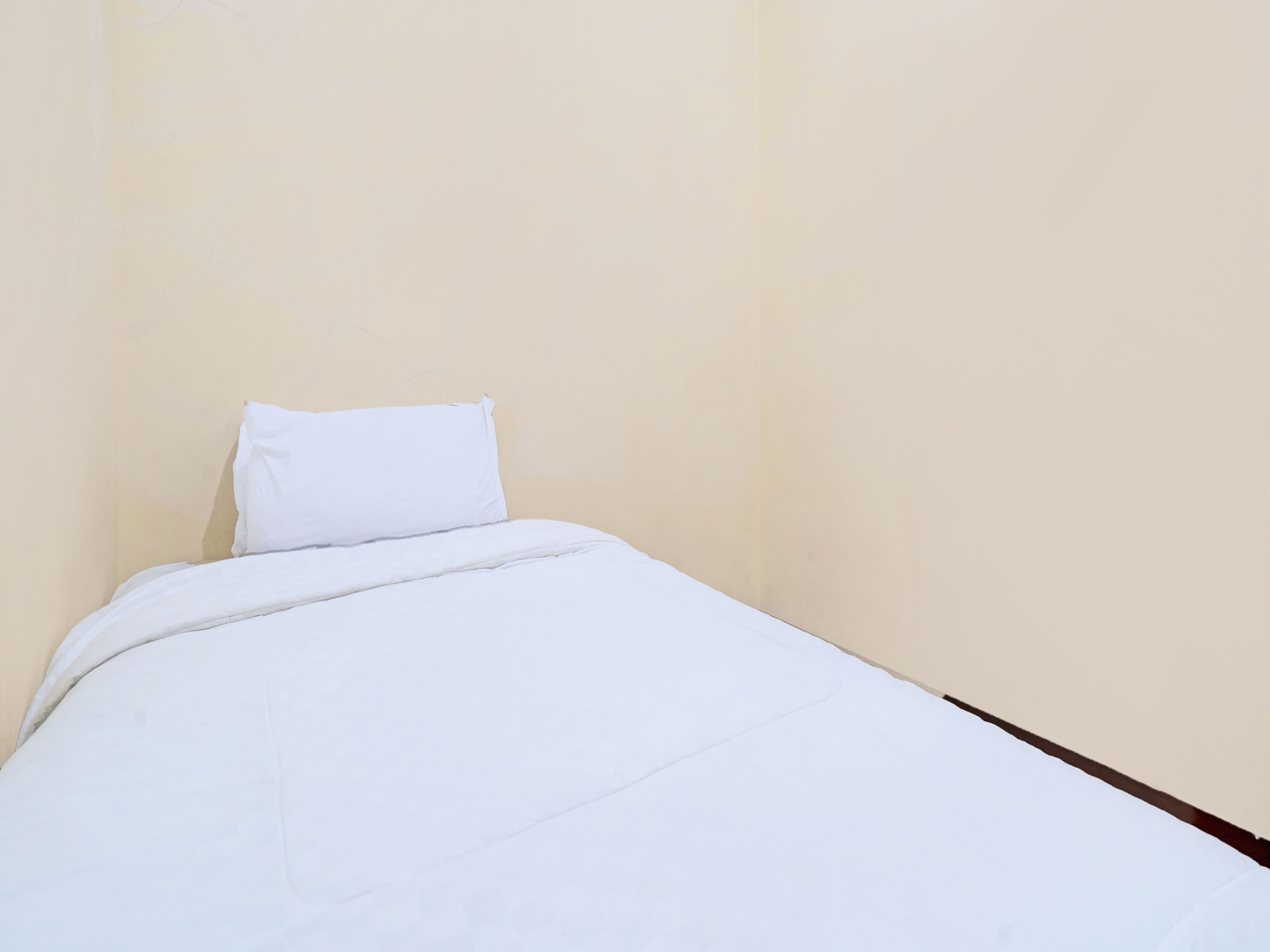 Une petite chambre avec un lit simple, recouverte d’une courtepointe blanche unie et agrémentée d’un seul oreiller blanc.
