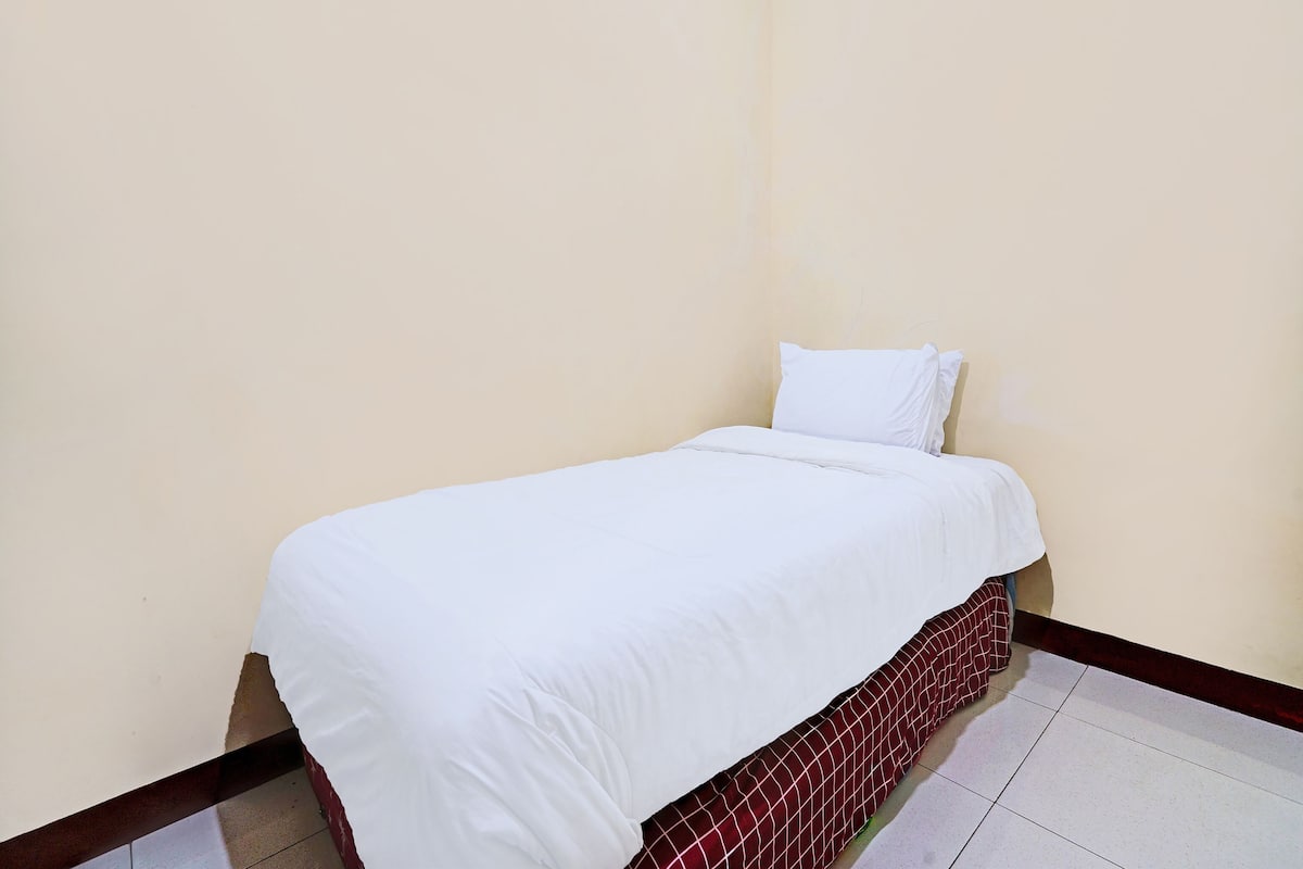 A single bed with white bedding in a room with plain walls and a tiled floor.