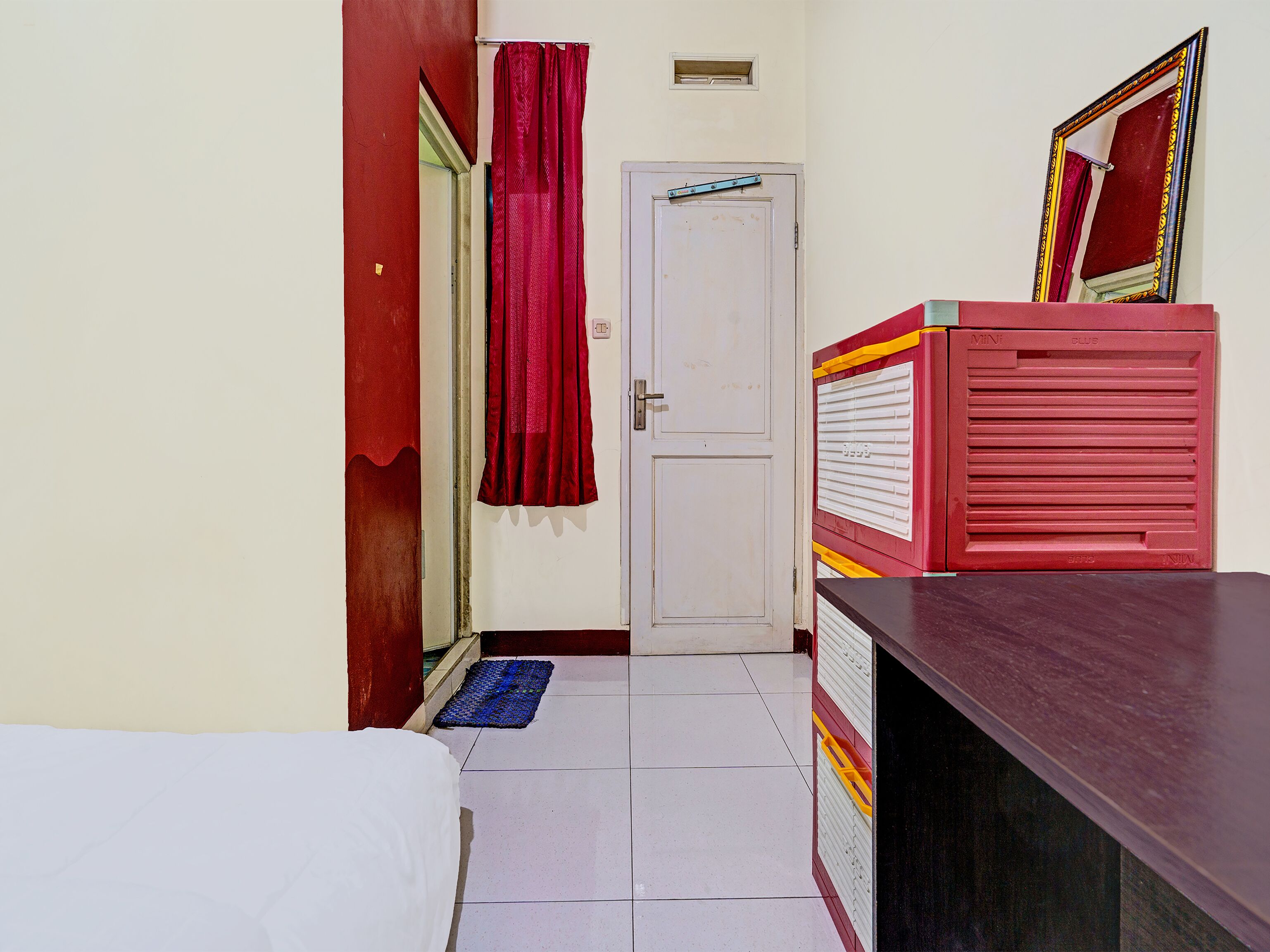 A room with a bed, a desk, a mirror, and a door.