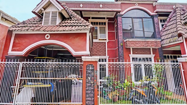 A multi-story house with a red facade, a gated front yard, and a balcony with a metal railing. - OYO Life 92546 Kost Merah Bojongsoang Syariah (Bojongsoang)