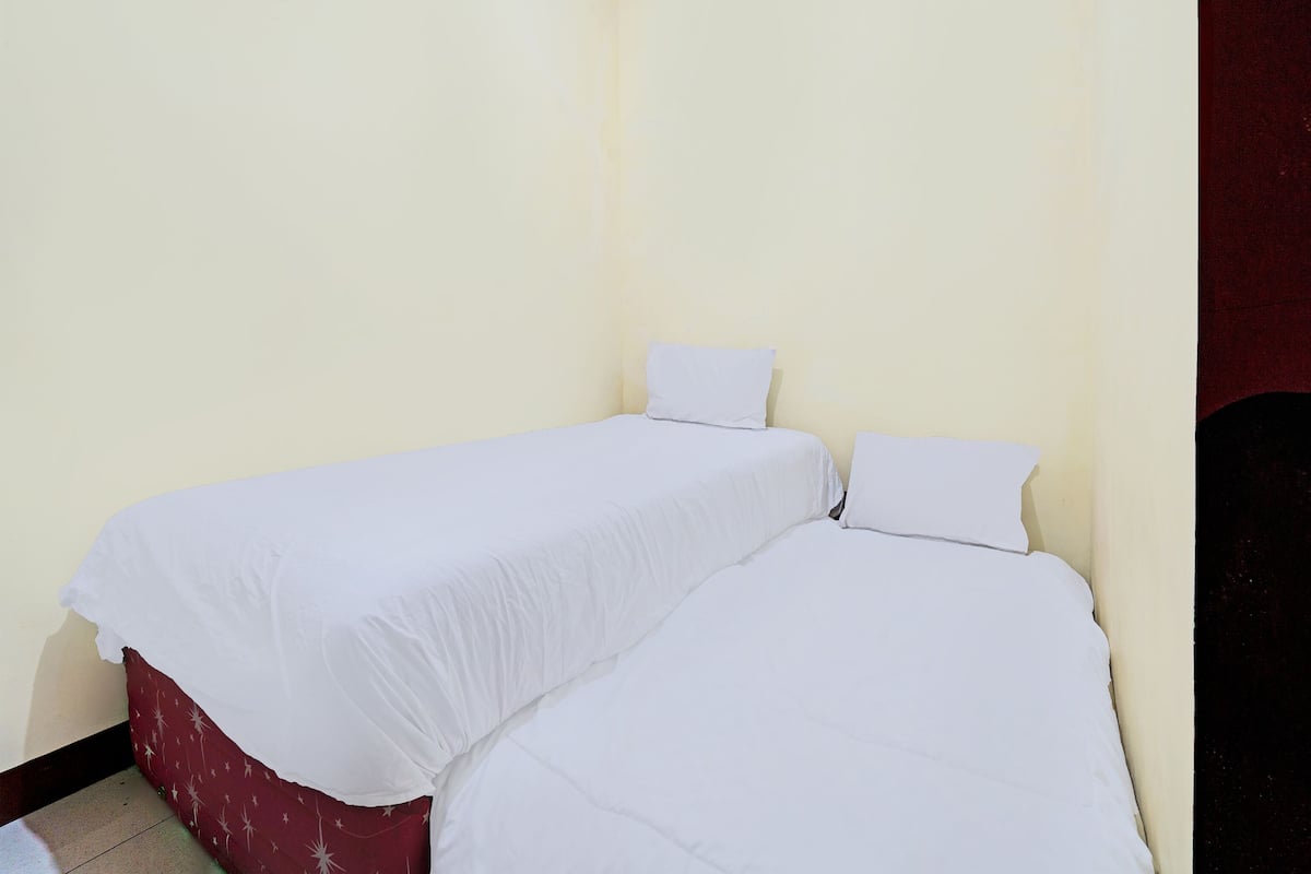 A small, single-room hotel room with two single beds, plain walls, and a tiled floor.
