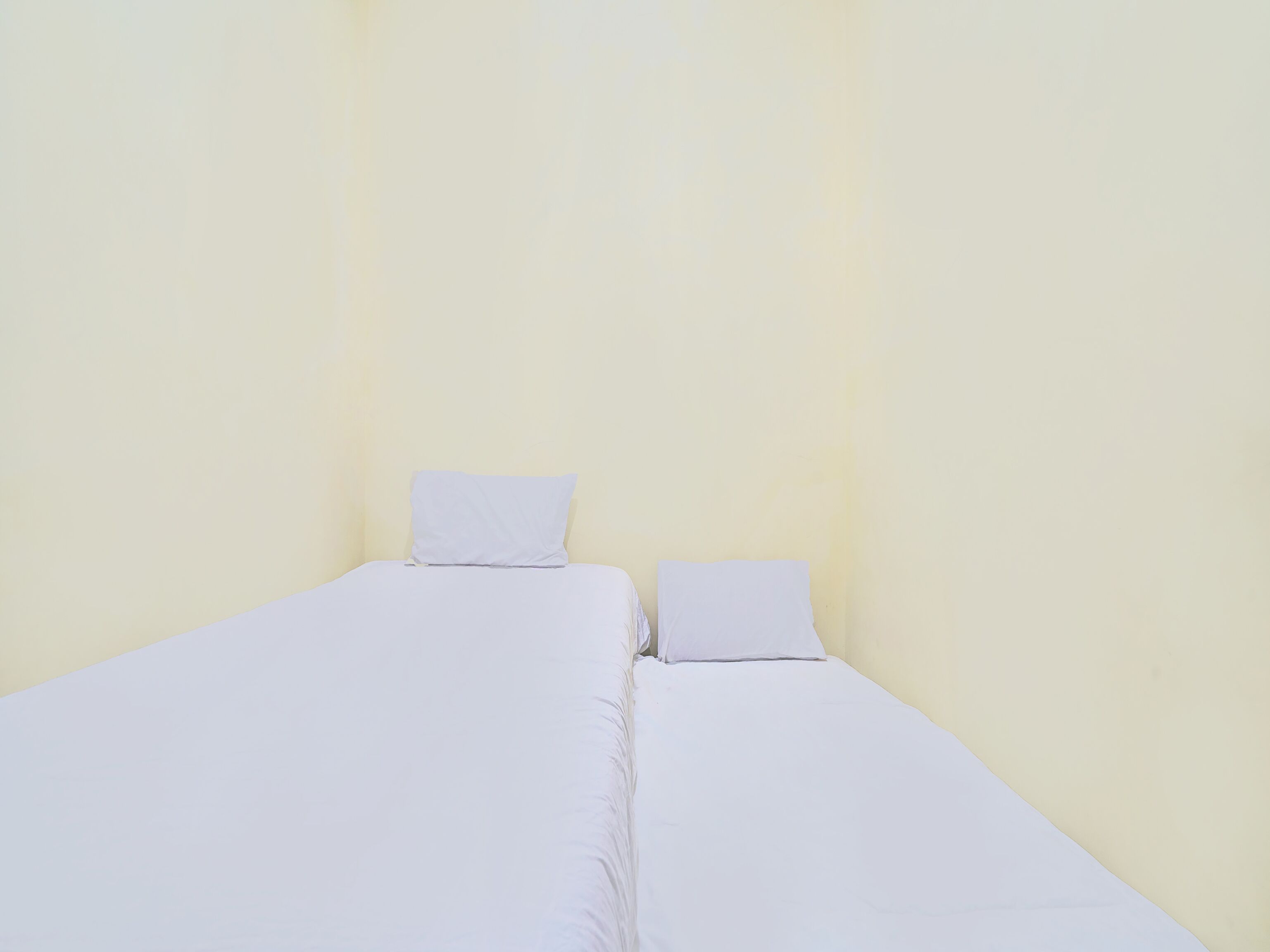 Une pièce simple et dépouillée, avec deux lits placés contre un mur uni.
