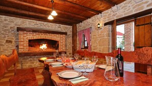 Un comedor rústico con chimenea de piedra, vigas de madera y una larga mesa de madera dispuesta para una comida.