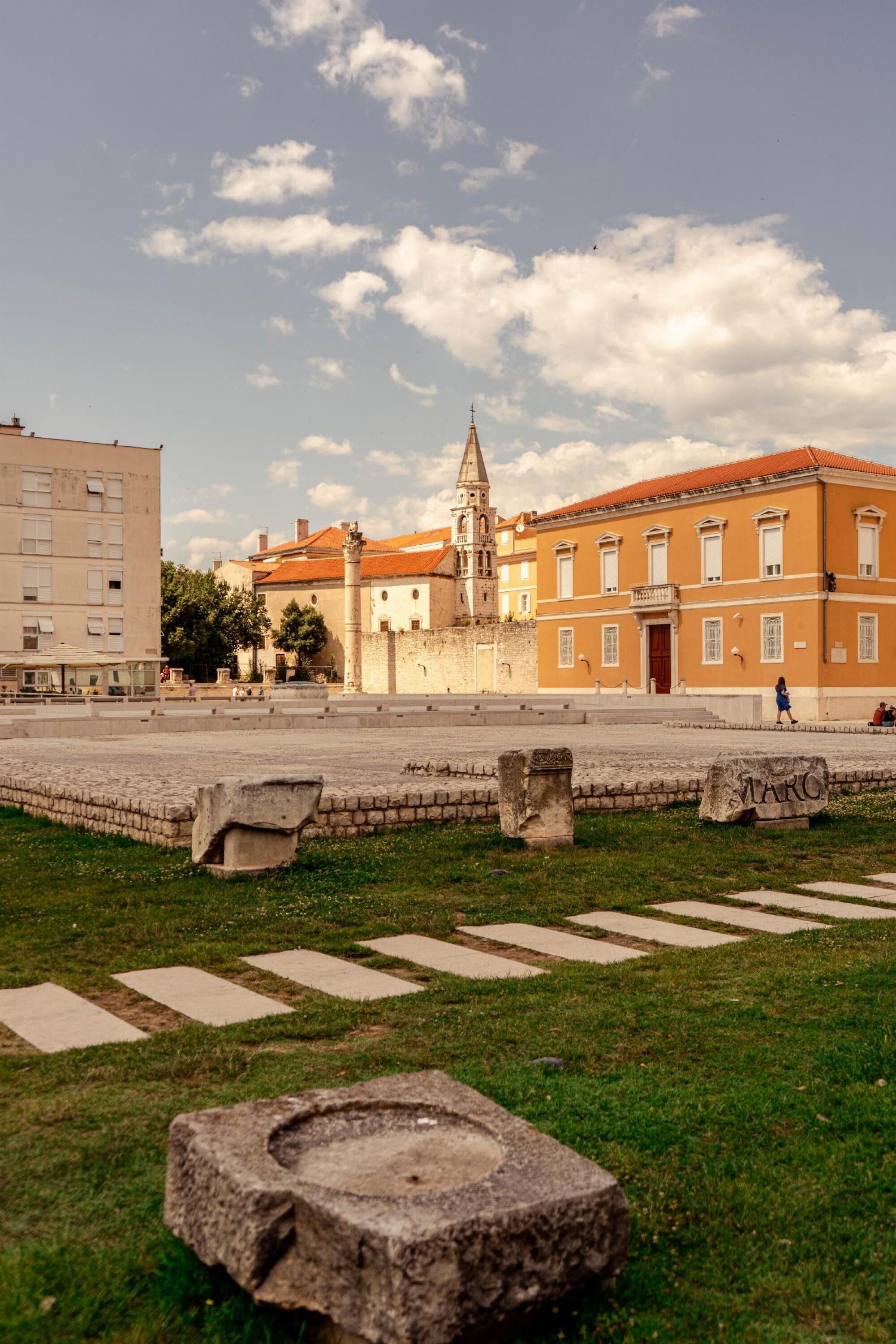 A square with a fountain, stone benches, and a historic building with a tower.