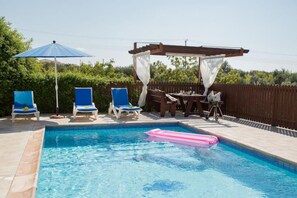 A swimming pool with blue and white lounge chairs, a wooden pergola, and a table with chairs. - Villa Sunlove in Peyia (Pegeia)