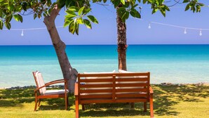 A wooden bench and chair under a tree by a clear blue sea. - Villa Sunlove in Peyia (Pegeia)